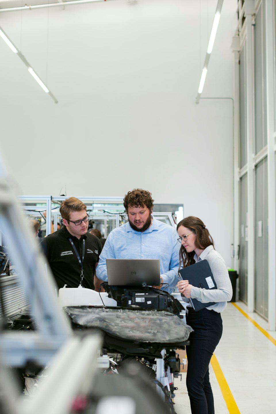 Professionals collaborate on a laptop in a modern industrial facility.